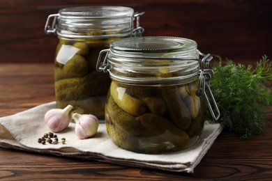 Pickled cucumbers in jars, garlic, dill and peppercorns on wooden table, closeup