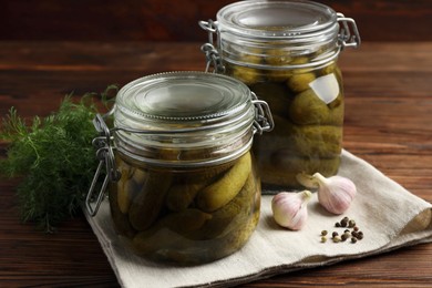 Pickled cucumbers in jars, garlic, dill and peppercorns on wooden table, closeup