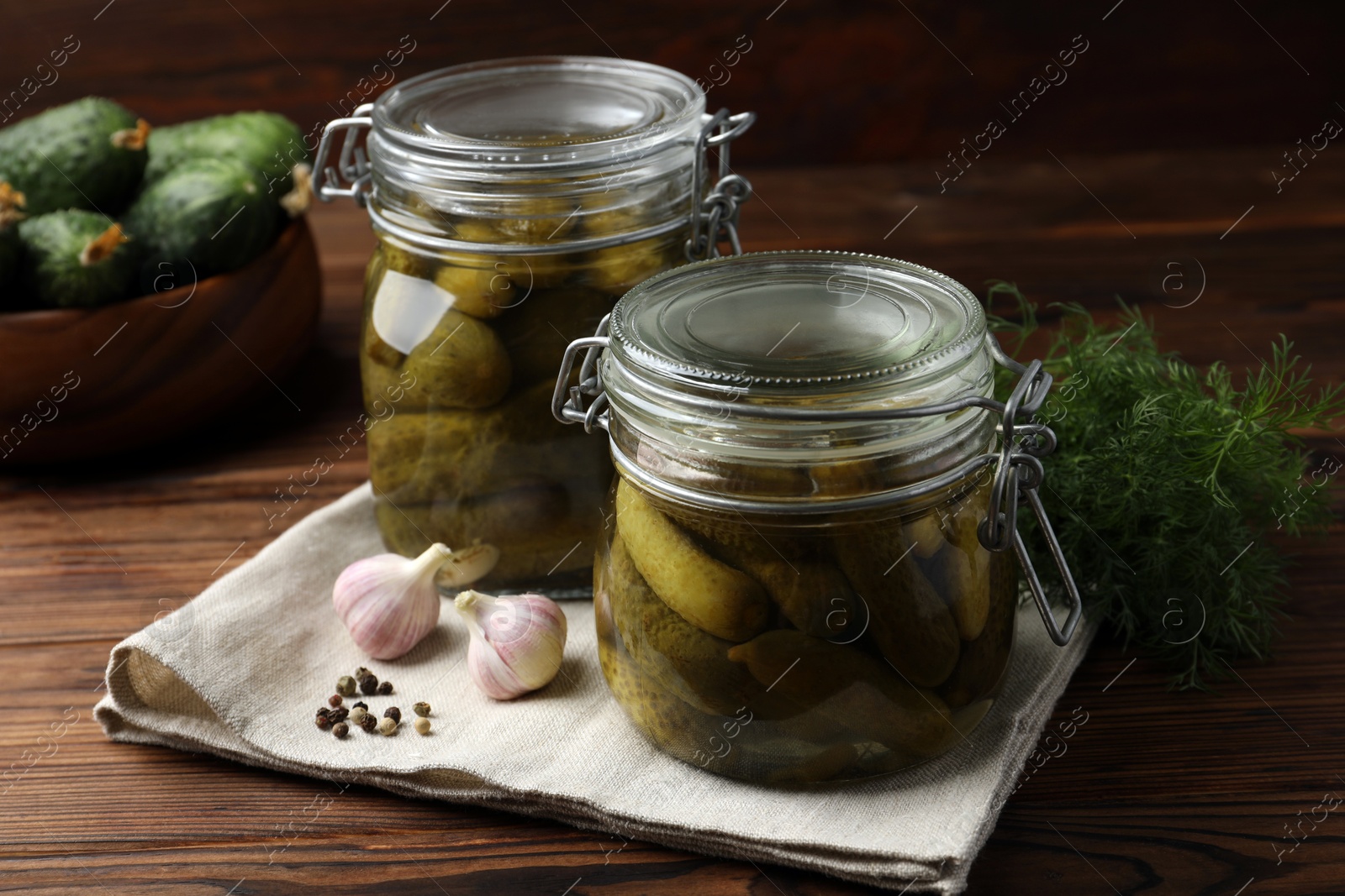 Photo of Pickled cucumbers in jars, garlic, dill and peppercorns on wooden table