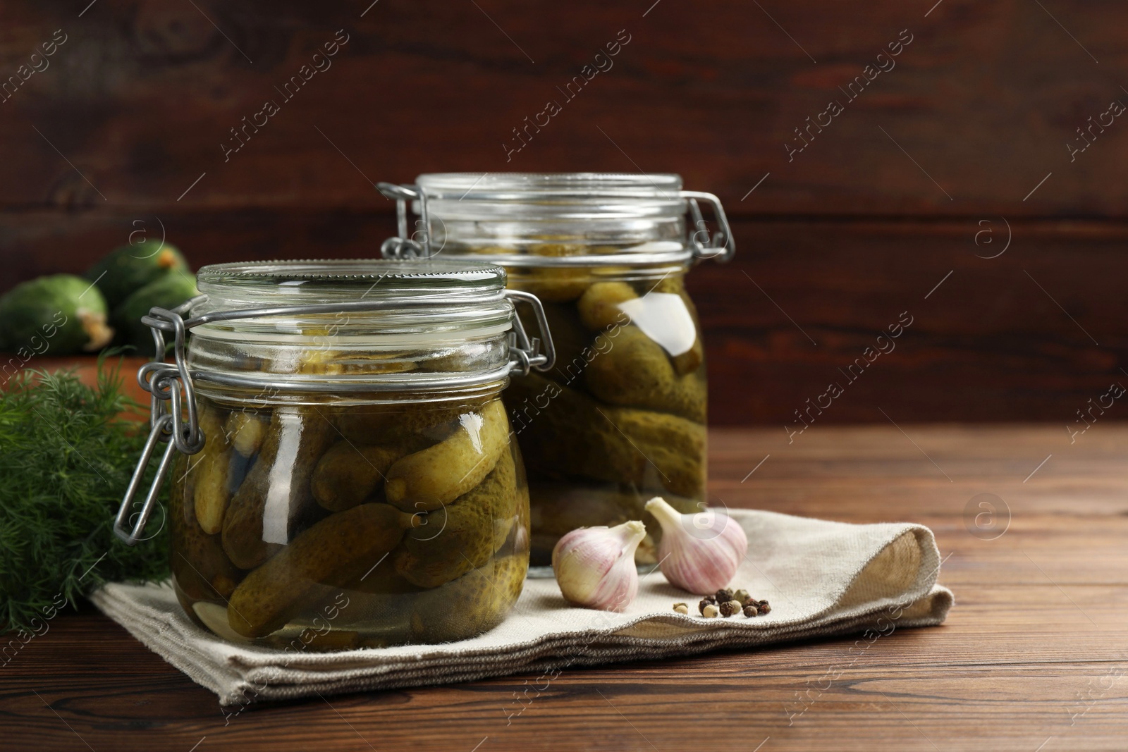 Photo of Pickled cucumbers in jars, garlic and dill on wooden table. Space for text