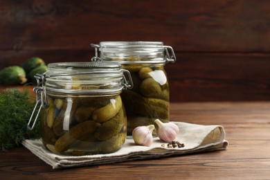 Pickled cucumbers in jars, garlic and dill on wooden table. Space for text