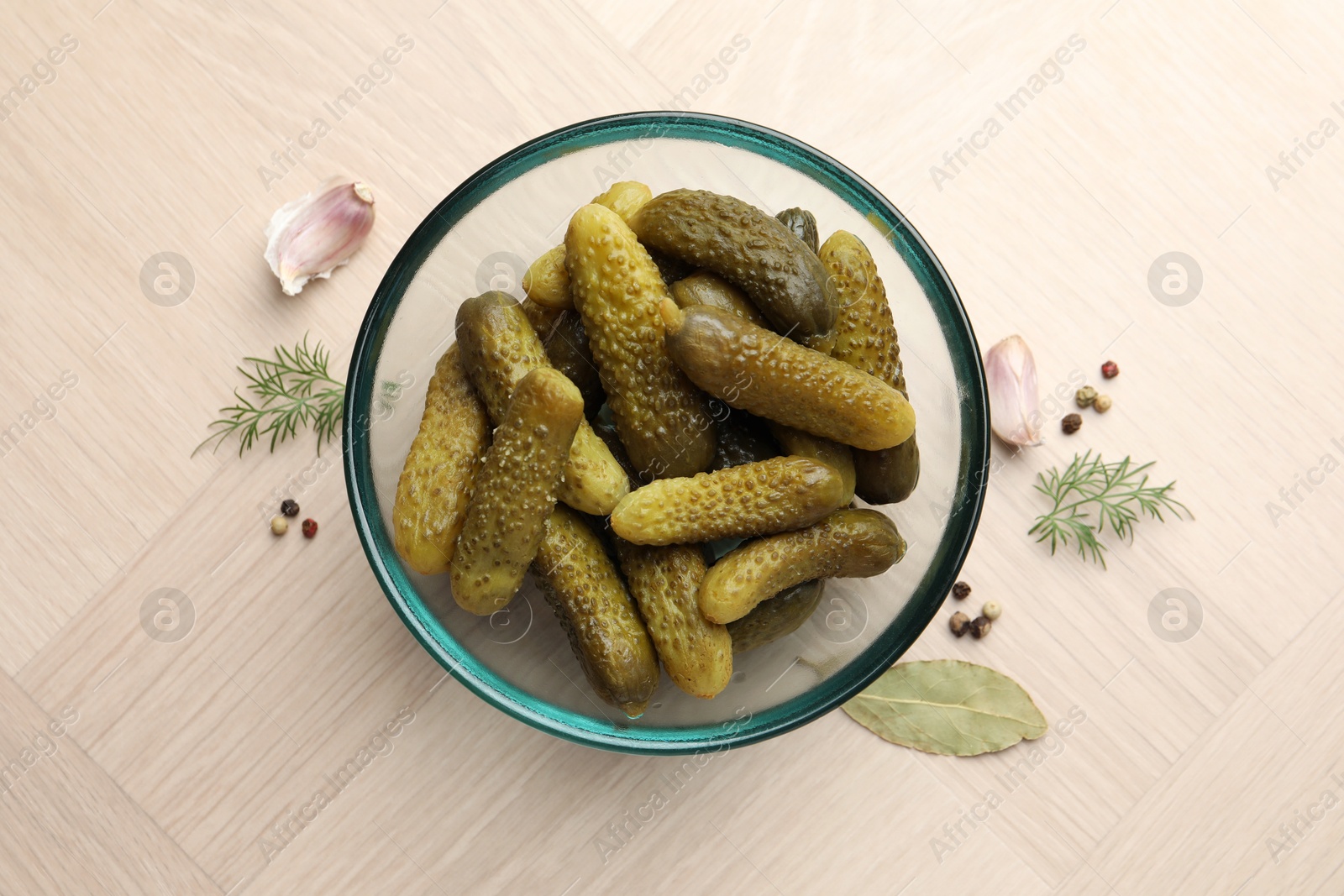 Photo of Pickled cucumbers in bowl and spices on light wooden table, flat lay