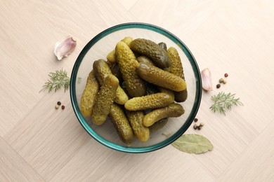 Pickled cucumbers in bowl and spices on light wooden table, flat lay