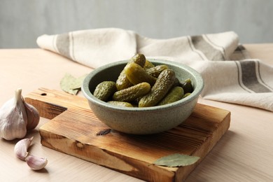 Photo of Pickled cucumbers in bowl, bay leaves and garlic on wooden table