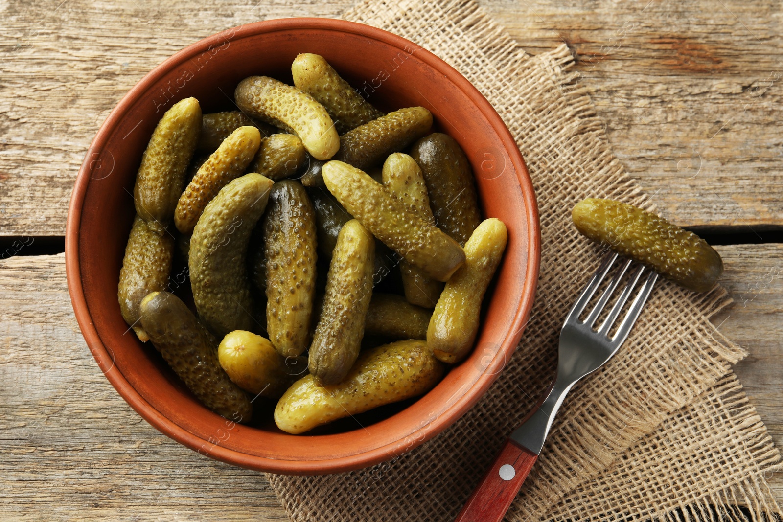 Photo of Pickled cucumbers in bowl and fork on wooden table, flat lay