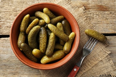 Pickled cucumbers in bowl and fork on wooden table, flat lay