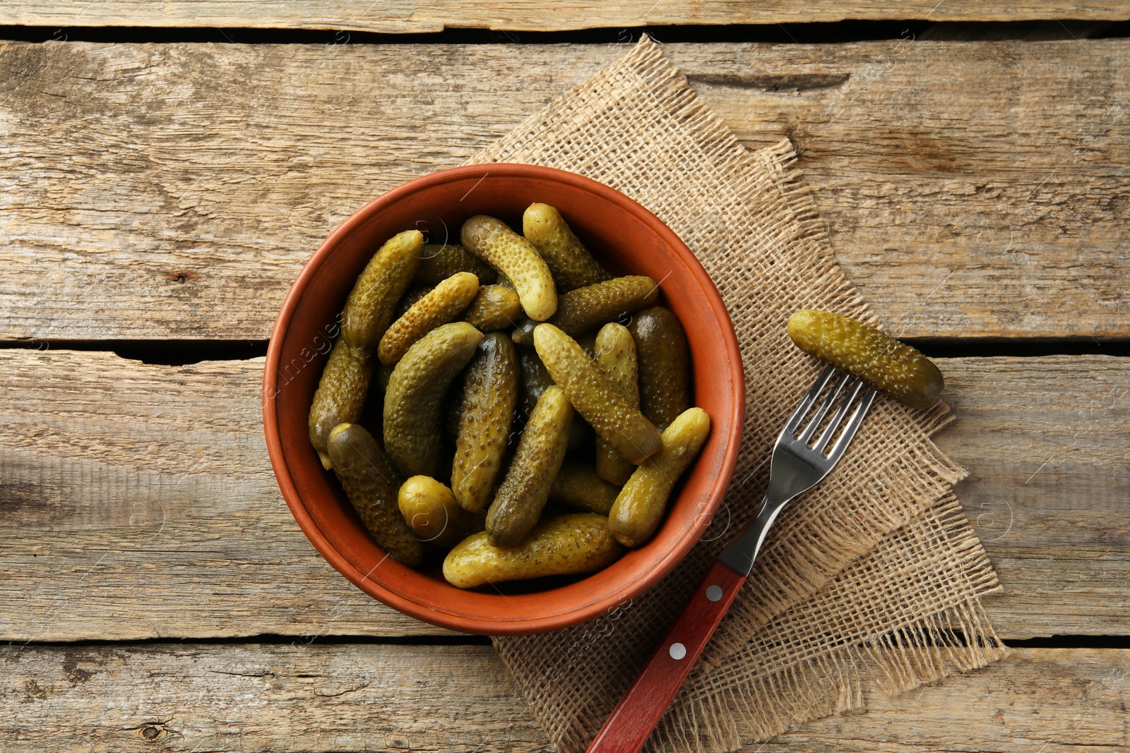 Photo of Pickled cucumbers in bowl and fork on wooden table, flat lay