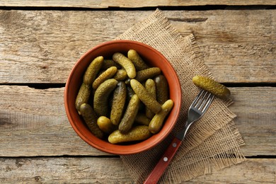 Pickled cucumbers in bowl and fork on wooden table, flat lay