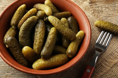 Pickled cucumbers in bowl and fork on wooden table, closeup