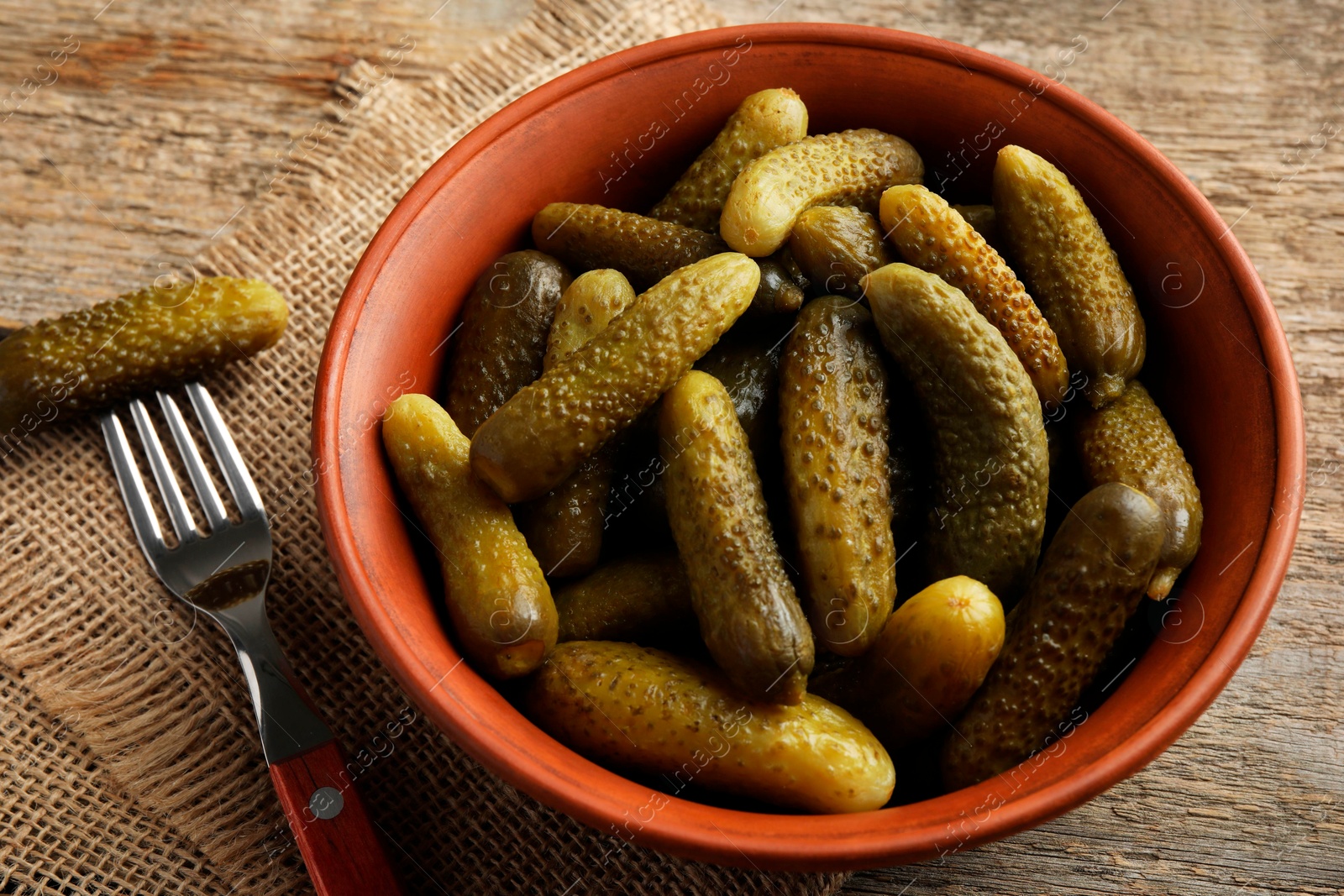 Photo of Pickled cucumbers in bowl and fork on wooden table, closeup