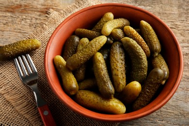 Pickled cucumbers in bowl and fork on wooden table, closeup