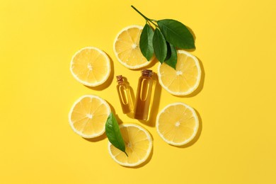 Photo of Bottles of essential oils, lemon and green leaves on yellow background, flat lay