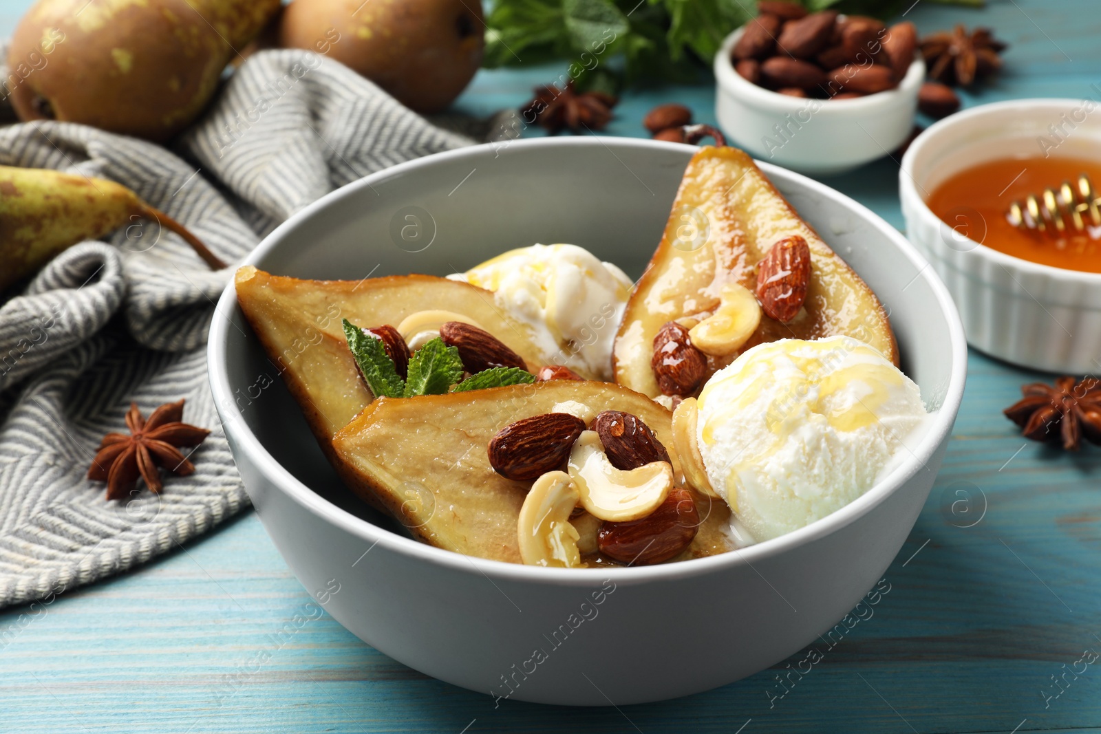 Photo of Delicious baked pears with nuts, ice cream and honey in bowl on light blue wooden table, closeup