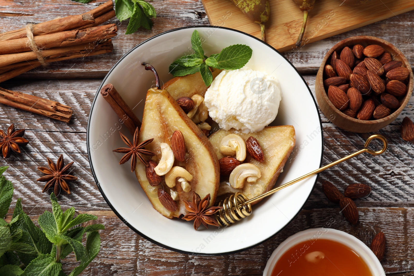 Photo of Delicious baked pears with nuts, ice cream, anise stars and honey in bowl on wooden rustic table, flat lay