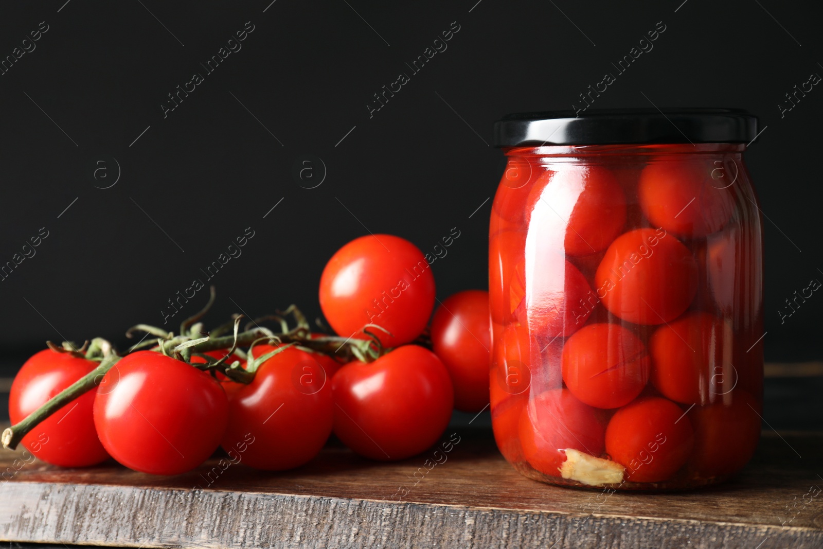 Photo of Tasty pickled tomatoes in jar and fresh vegetables on wooden table