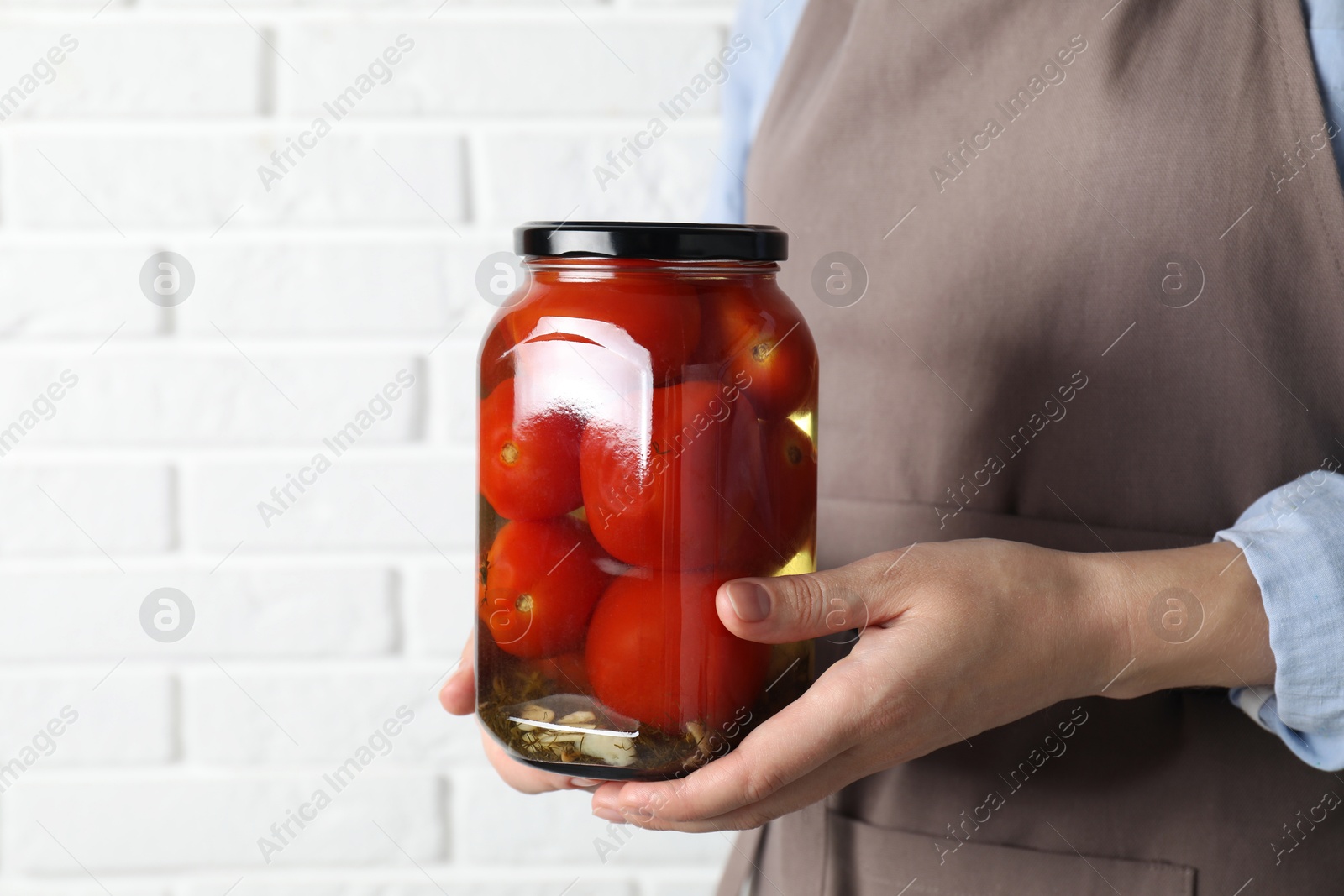 Photo of Woman holding jar with tasty pickled tomatoes against white brick wall, closeup. Space for text