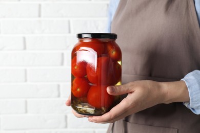 Woman holding jar with tasty pickled tomatoes against white brick wall, closeup. Space for text