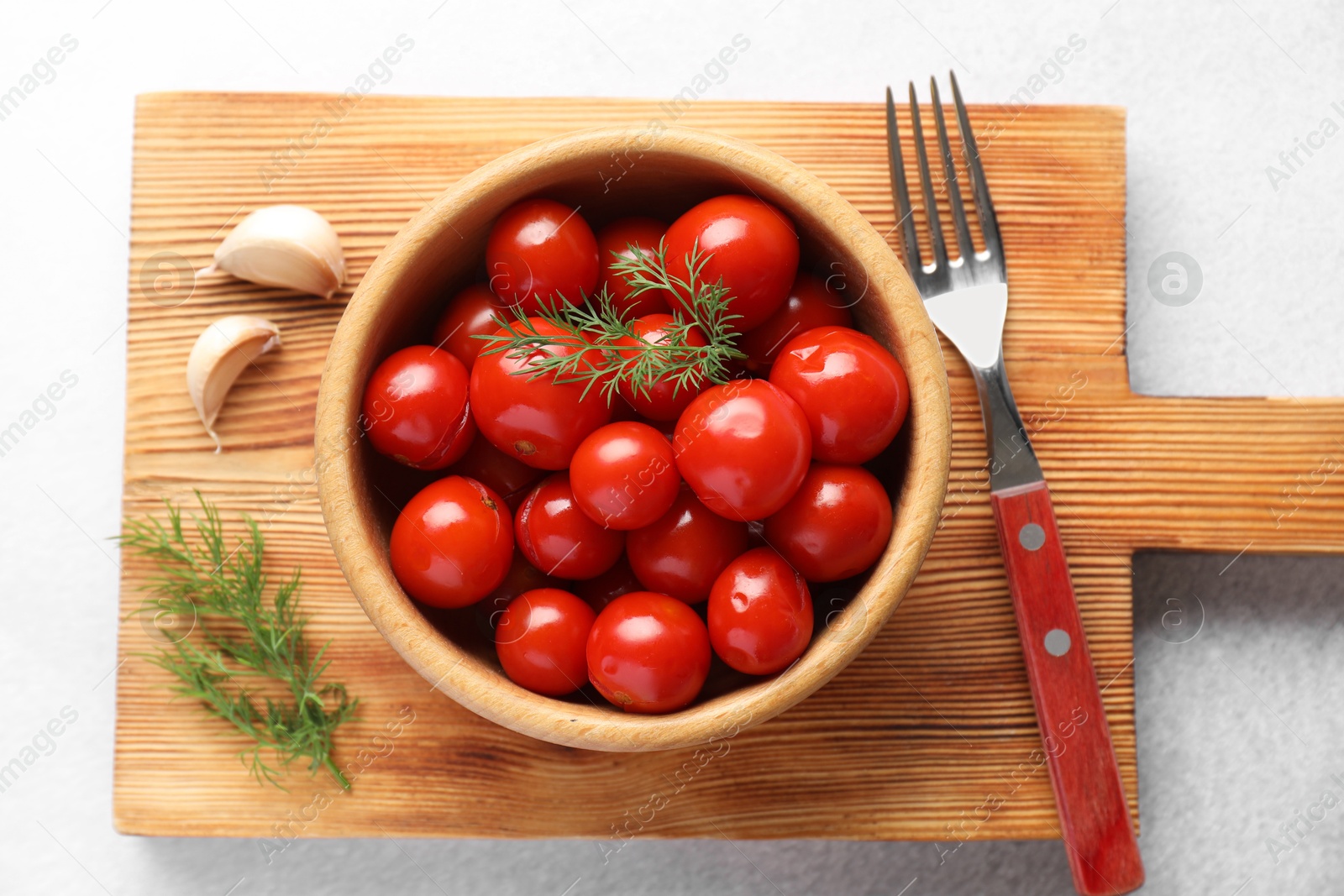 Photo of Tasty pickled tomatoes in bowl, dill, garlic and fork on white table, top view