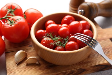 Photo of Tasty pickled tomatoes in bowl, fresh vegetables, dill, garlic and fork on table