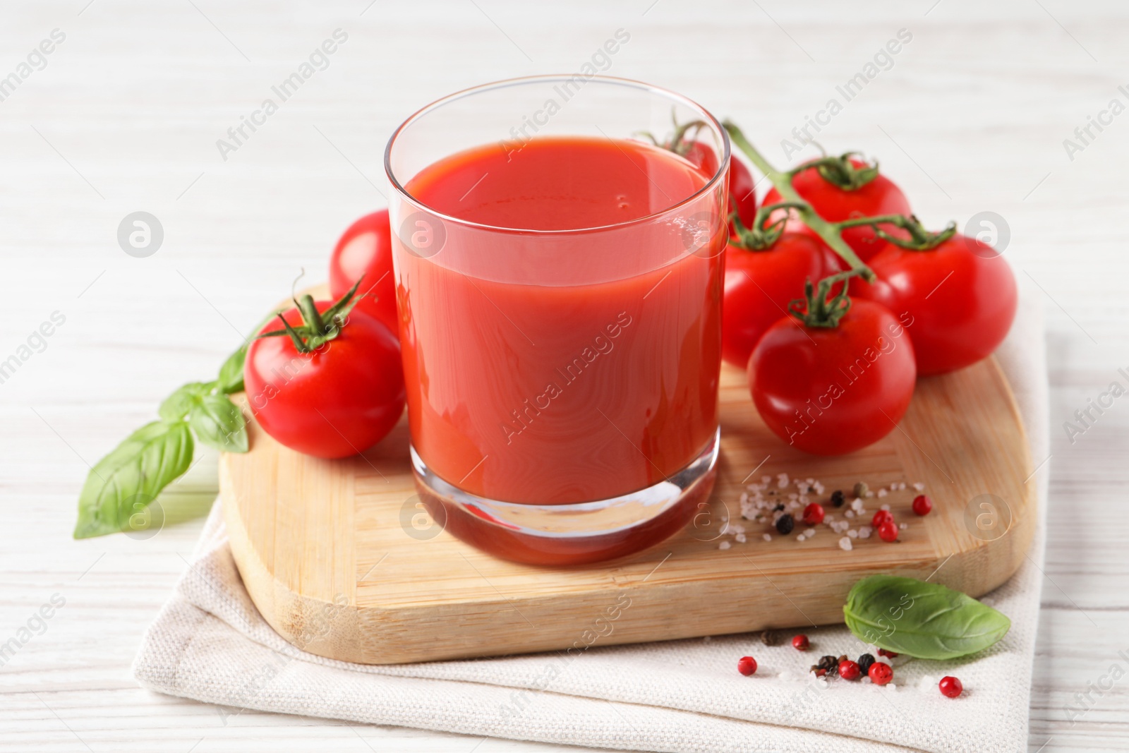 Photo of Tasty tomato juice in glass with fresh vegetables and spices on white wooden table