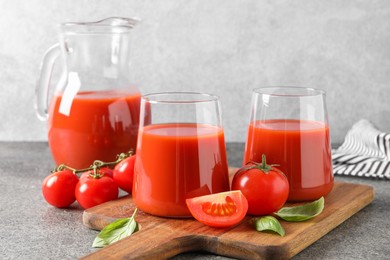 Tasty tomato juice in glasses, basil and fresh vegetables on grey table