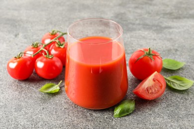 Photo of Tasty tomato juice in glass, basil and fresh vegetables on grey table