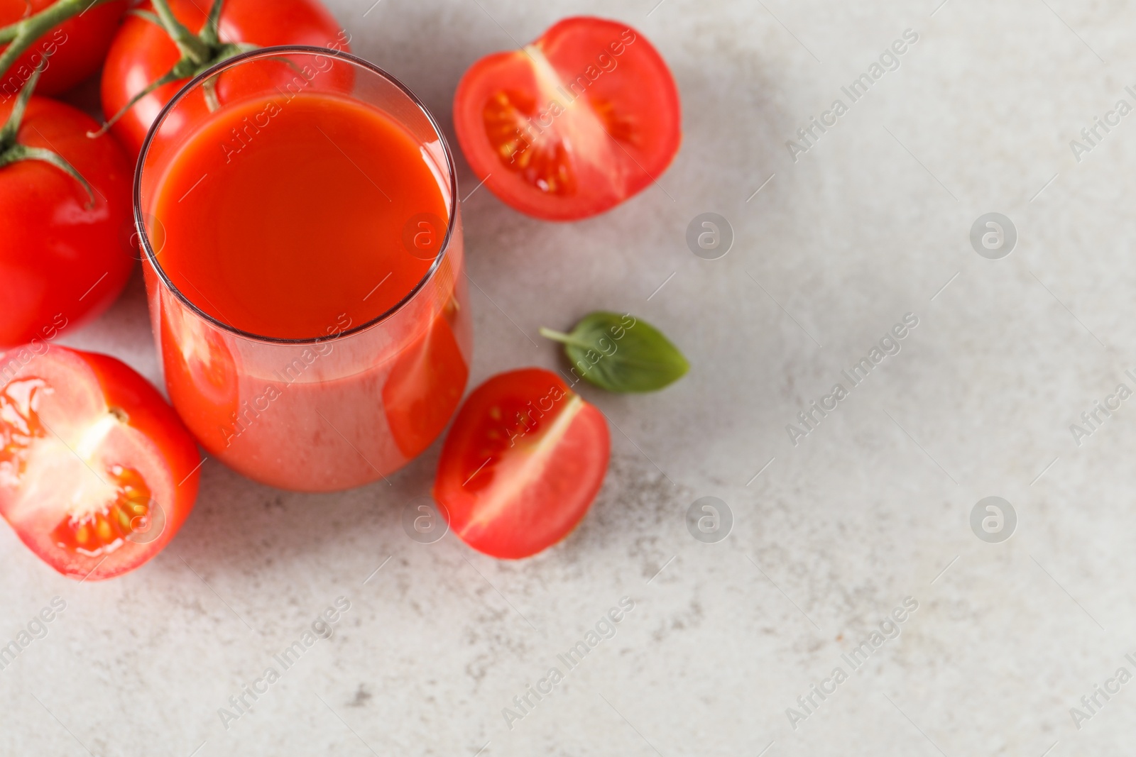 Photo of Tasty tomato juice in glass, basil and fresh vegetables on light grey table, space for text