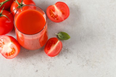 Photo of Tasty tomato juice in glass, basil and fresh vegetables on light grey table, space for text