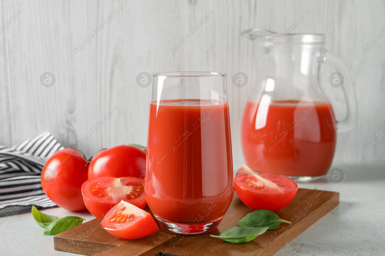 Photo of Tasty tomato juice in glass, basil leaves and fresh vegetables on light grey table