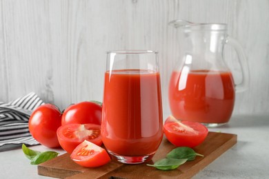 Tasty tomato juice in glass, basil leaves and fresh vegetables on light grey table