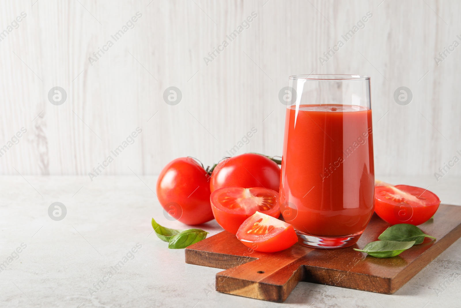 Photo of Tasty tomato juice in glass, basil leaves and fresh vegetables on light grey table, space for text