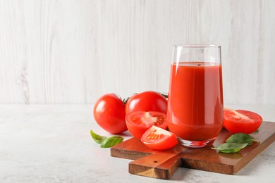 Photo of Tasty tomato juice in glass, basil leaves and fresh vegetables on light grey table, space for text