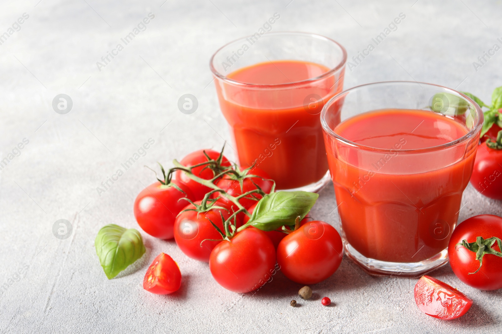 Photo of Tasty tomato juice in glasses, basil leaves, fresh vegetables and peppercorns on light grey table