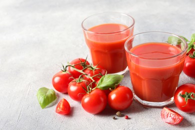 Photo of Tasty tomato juice in glasses, basil leaves, fresh vegetables and peppercorns on light grey table