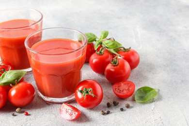 Photo of Tasty tomato juice in glasses, basil leaves, fresh vegetables and peppercorns on light grey table