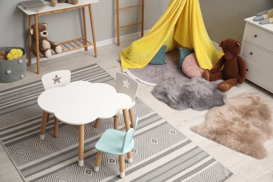 Photo of Stylish child room interior with table, chairs, toys and play tent