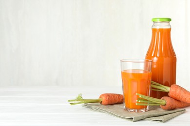 Photo of Healthy juice and fresh carrot on white wooden table. Space for text