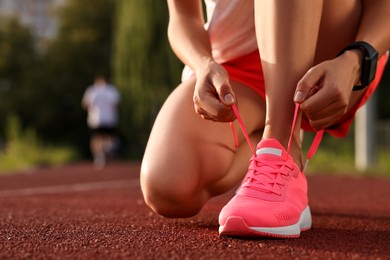 Photo of Woman tying shoelace of pink sneaker at stadium, closeup. Space for text