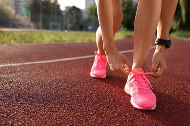 Woman tying shoelace of pink sneaker at stadium, closeup. Space for text