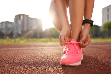 Photo of Woman tying shoelace of pink sneaker at stadium, closeup. Space for text