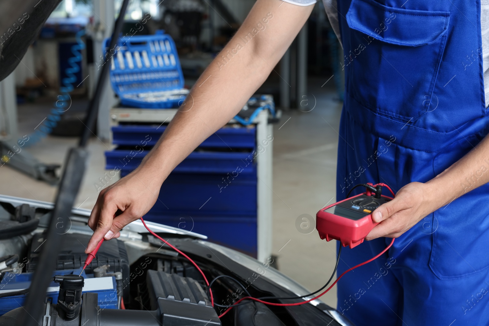 Photo of Auto mechanic with multimeter doing diagnostic at automobile repair shop, closeup