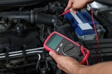 Photo of Auto mechanic with multimeter doing diagnostic at automobile repair shop, closeup