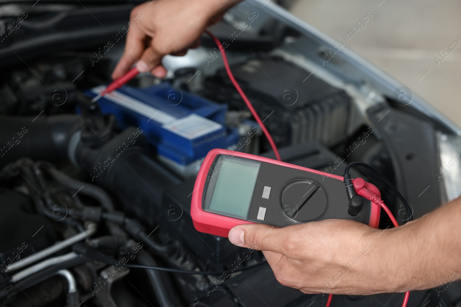 Photo of Auto mechanic with multimeter doing diagnostic at automobile repair shop, closeup