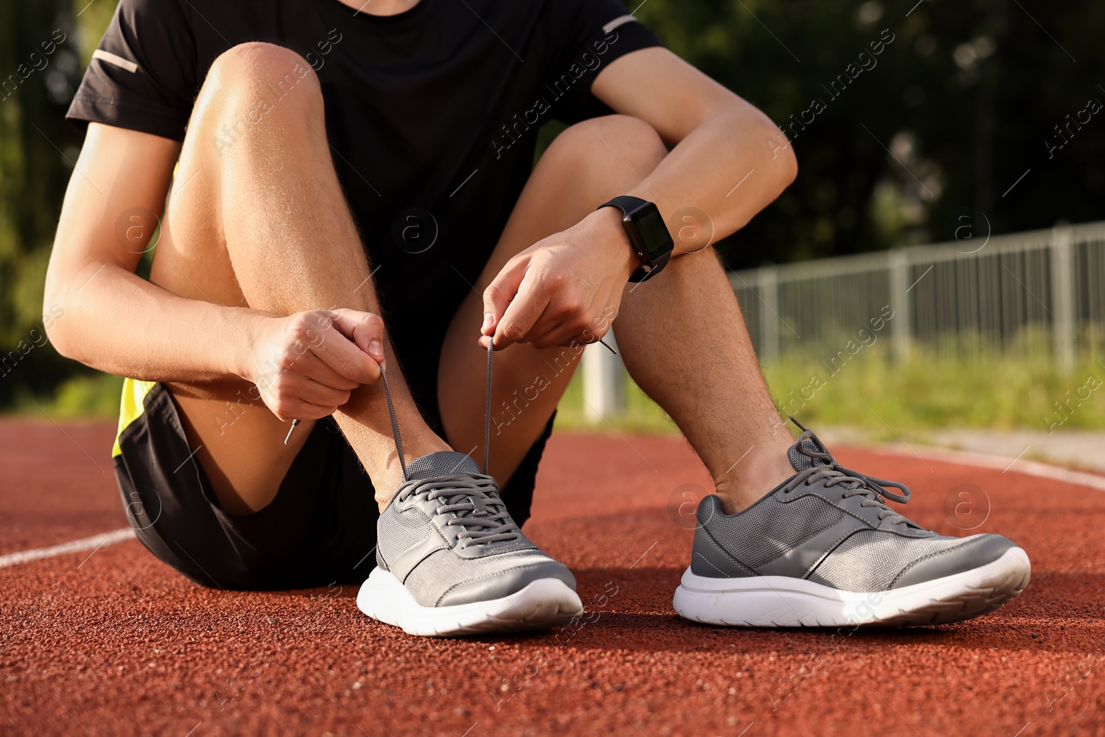 Photo of Man tying shoelace of grey sneaker at stadium, closeup