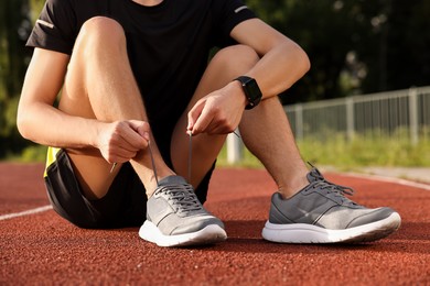 Photo of Man tying shoelace of grey sneaker at stadium, closeup