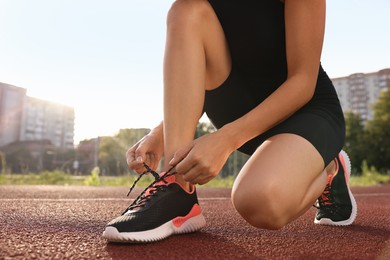 Woman tying shoelace of sneaker at stadium, closeup