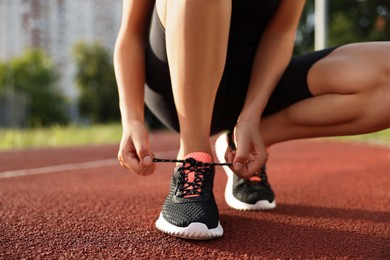 Woman tying shoelace of sneaker at stadium, closeup