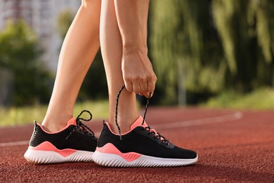 Photo of Woman tying shoelace of sneaker at stadium, closeup. Space for text