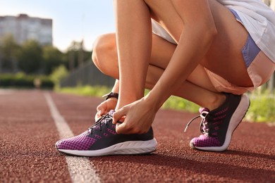 Photo of Woman tying shoelace of sneaker at stadium, closeup