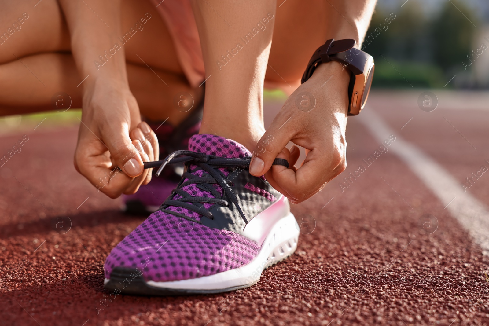 Photo of Woman tying shoelace of sneaker at stadium, closeup